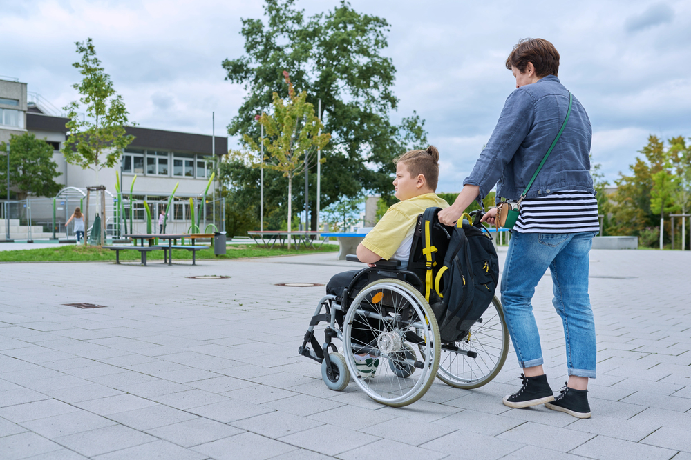 Back view of woman with boy in wheelchair near the school building.//Depositphotos